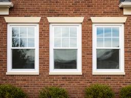 New white-framed replacement windows installed on a brick home